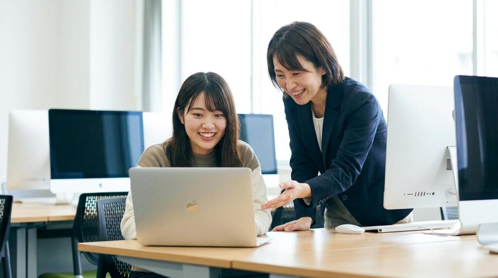 明るいパソコン教室で、AIの効率性に驚き喜ぶ日本人の女性生徒と、隣で優しく指導する講師。